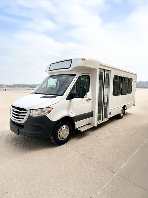 white shuttle bus in large parking lot area with a cityscape far behind it.